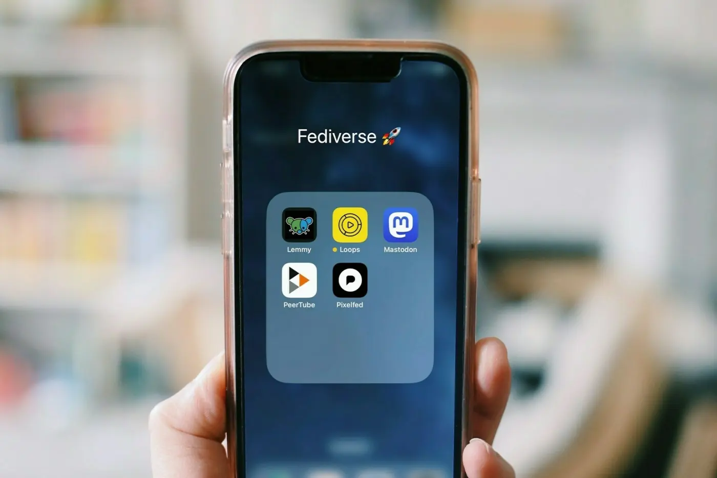 A hand holding a smartphone. The screen shows a folder of Fediverse apps.
