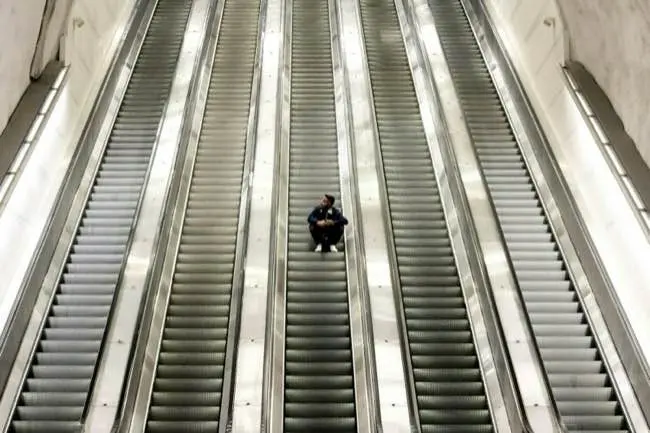 Auto-generated description: A person is sitting on the steps of a wide, empty escalator.