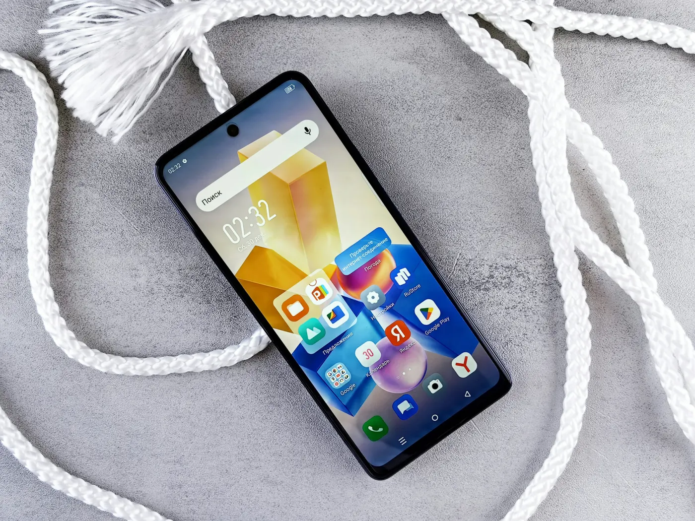 Auto-generated description: A smartphone with a colorful home screen lies on a textured gray surface surrounded by white ropes.