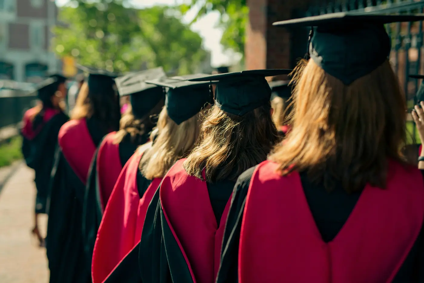 Auto-generated description: A group of graduates in black caps and gowns with red stoles walk in a line.