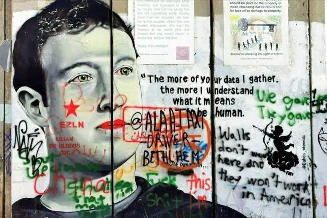 A mural featuring Mark Zuckerberg's face is covered by various graffiti, including a quote about data and humanity, political symbols, and colourful tags.