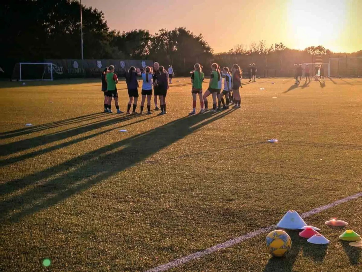 A training session in progress on an artificial pitch with sunset in the background and long shadows