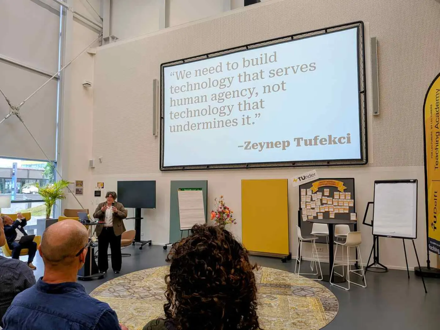 Kerri Lemoie presenting at the DCC Summit. There is a large quotation on the screen behind er from Zeynep Tufekci saying "We need to build technology that serves human agency, not technology that undermines it."
