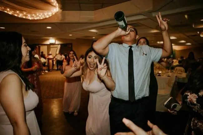 Auto-generated description: A group of people are celebrating at a party, with one person drinking from a bottle and others posing with peace signs.