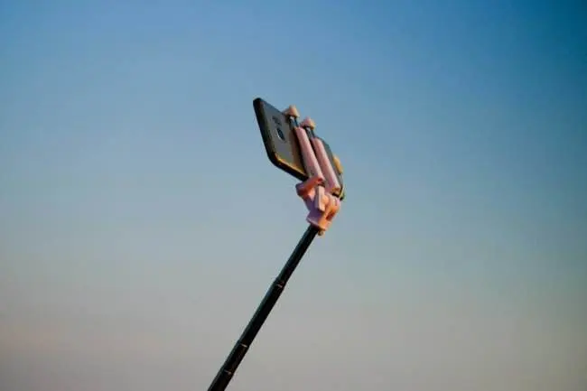 Auto-generated description: A smartphone is mounted on a selfie stick against a clear blue sky.