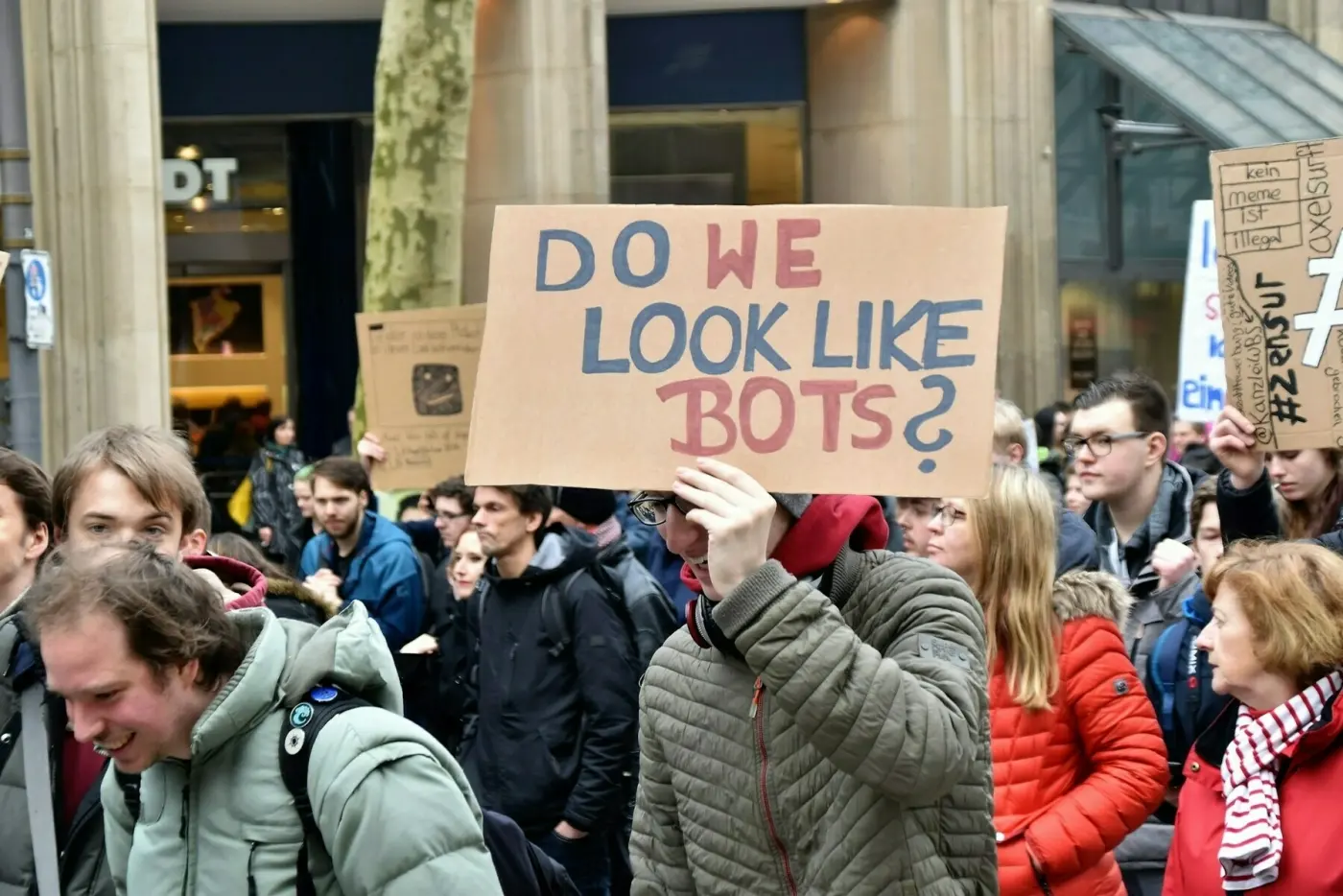 Crowd with person holding sign saying 'Do we look like bots?'