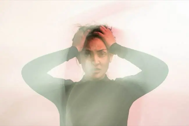 A person appears in a state of distress with hands on their head, surrounded by a blurred, translucent effect.
