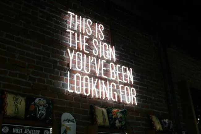 Auto-generated description: A neon sign on a brick wall displays the text THIS IS THE SIGN YOU'VE BEEN LOOKING FOR.