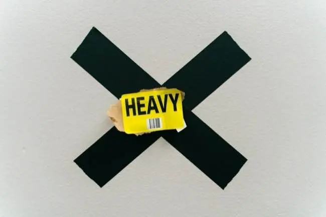 A black X is marked on a surface with a yellow label that says 'HEAVY' placed over it.