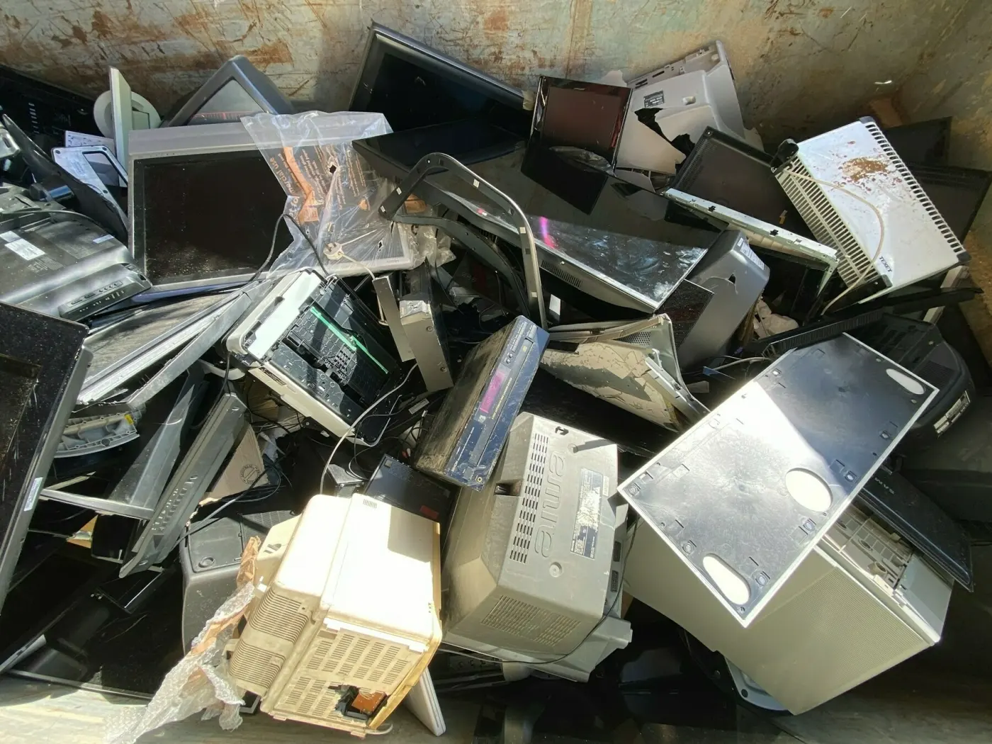Auto-generated description: A pile of discarded electronic waste, including old monitors and computers, is scattered in a container.