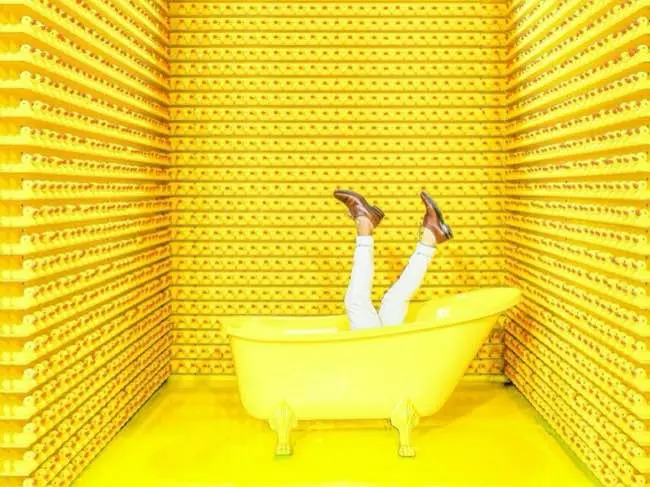 Very yellow image depicting a person in a bathtub with their legs in the air. Their torso cannot be seen.