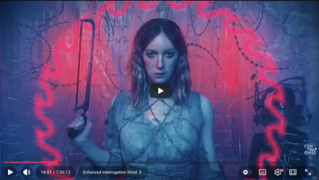 Auto-generated description: A person stands in front of a wire fence, illuminated by red and blue lighting, holding a whip-like object, creating a dramatic and intense atmosphere.