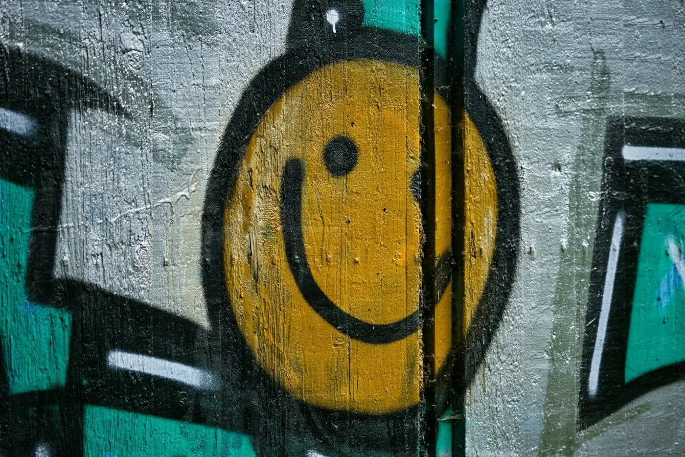 Auto-generated description: A yellow smiley face is painted on a textured wall with abstract graffiti elements in the background.