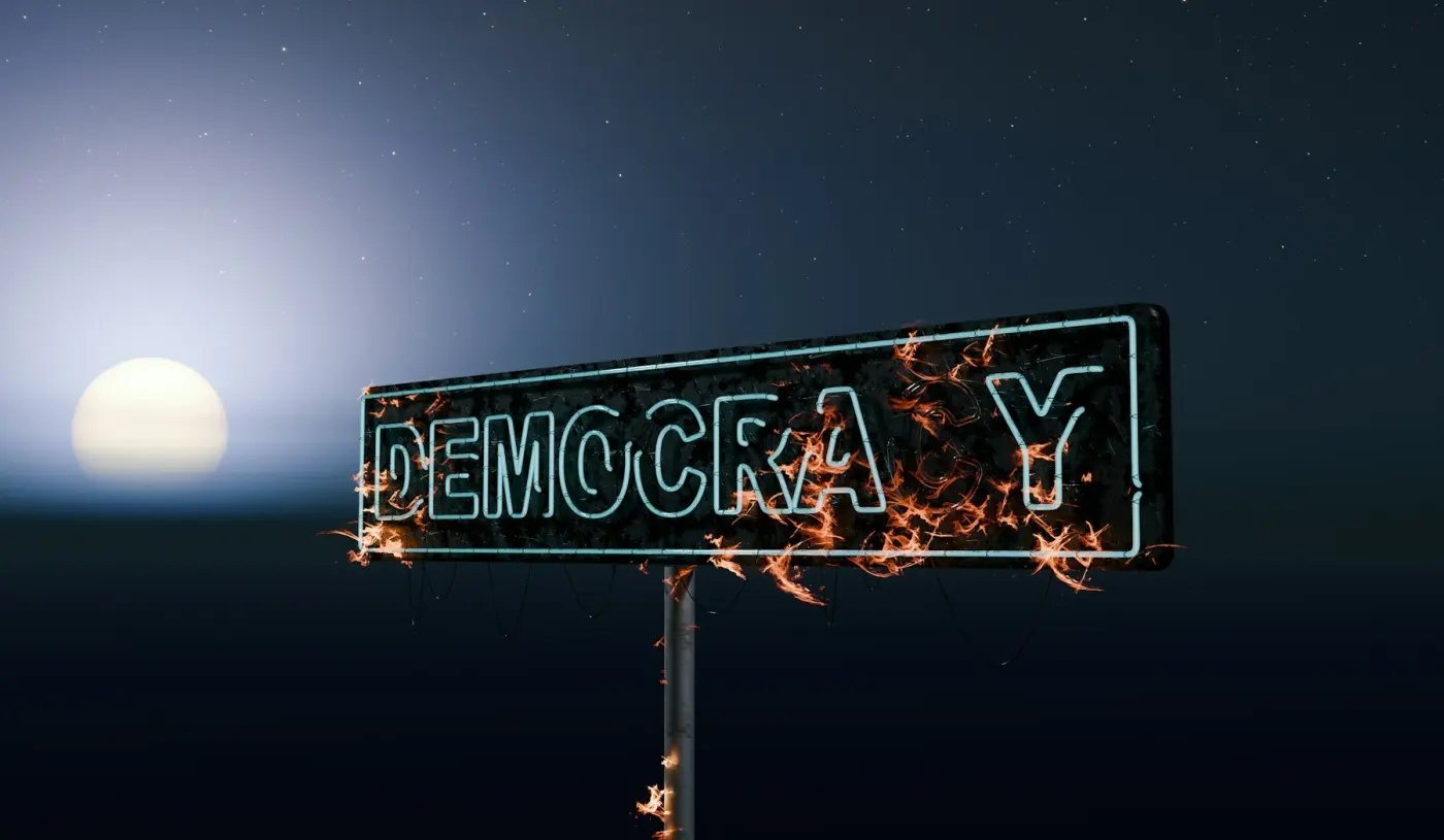 Auto-generated description: A neon sign spelling out DEMOCRACY with the Y on fire is set against a night sky with a visible glowing moon.