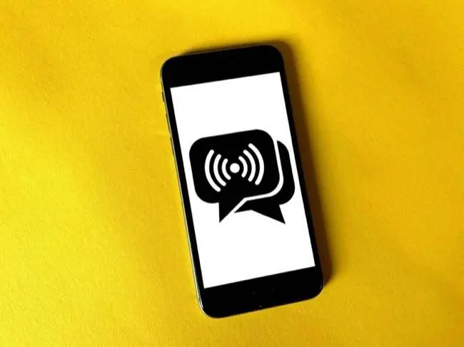 Auto-generated description: A smartphone displaying a speech bubble icon with broadcast signal waves is set against a bright yellow background.