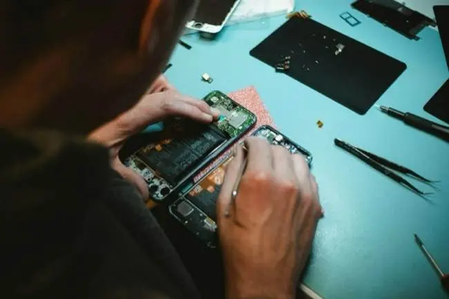 Auto-generated description: A person is repairing or examining a smartphone on a workbench with various tools and components around them.