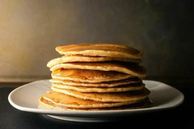 Auto-generated description: A stack of golden-brown pancakes is neatly arranged on a white plate.