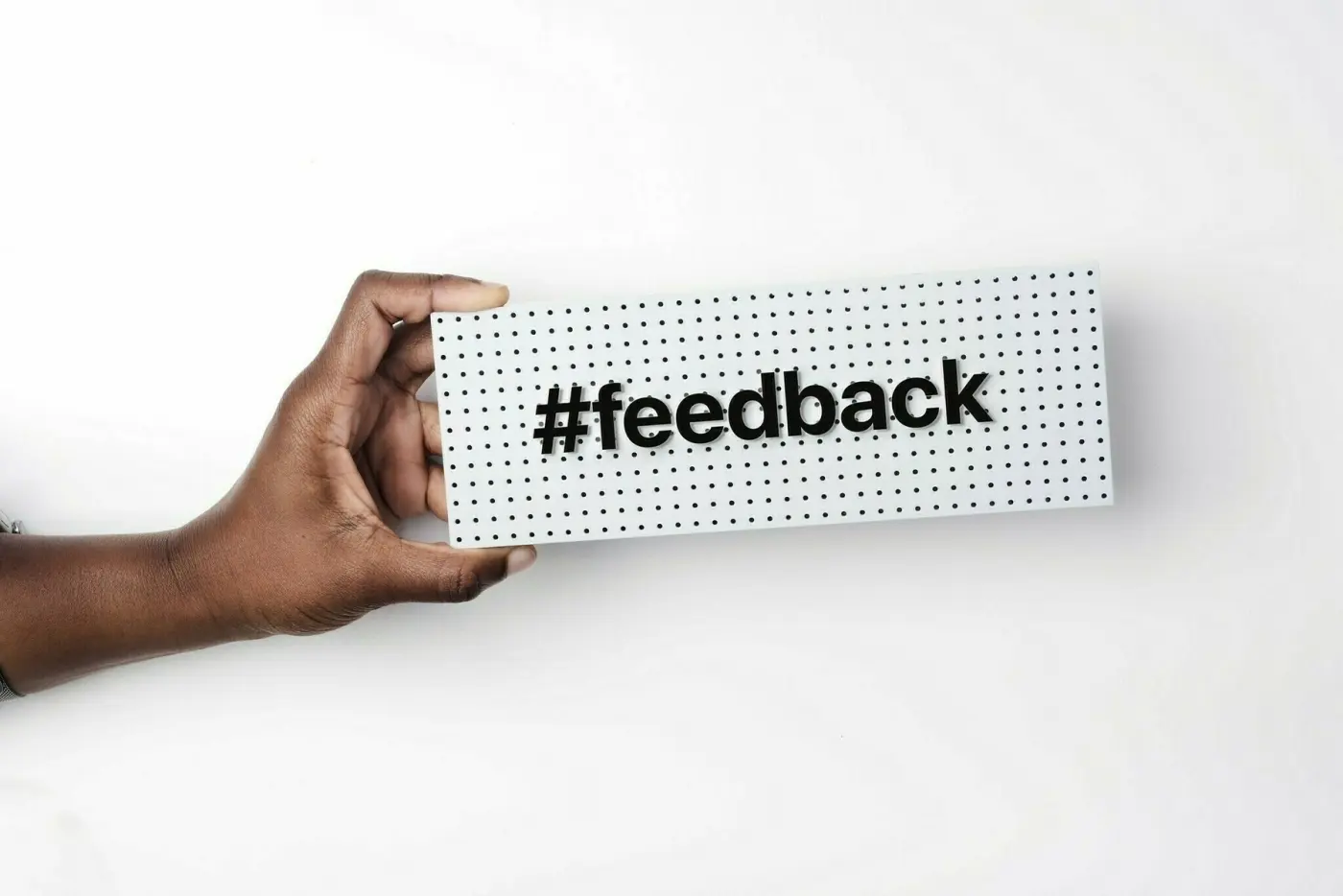 Auto-generated description: A hand is holding a perforated board with the word #feedback on it.