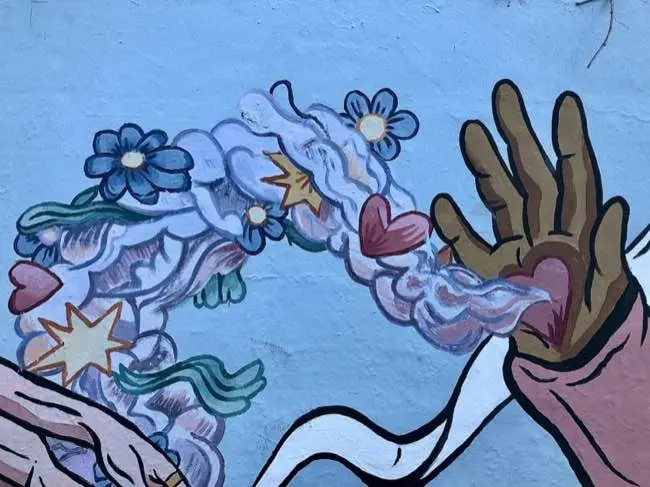 Auto-generated description: A mural depicts a hand releasing a colorful swirl of flowers, hearts, and abstract shapes.