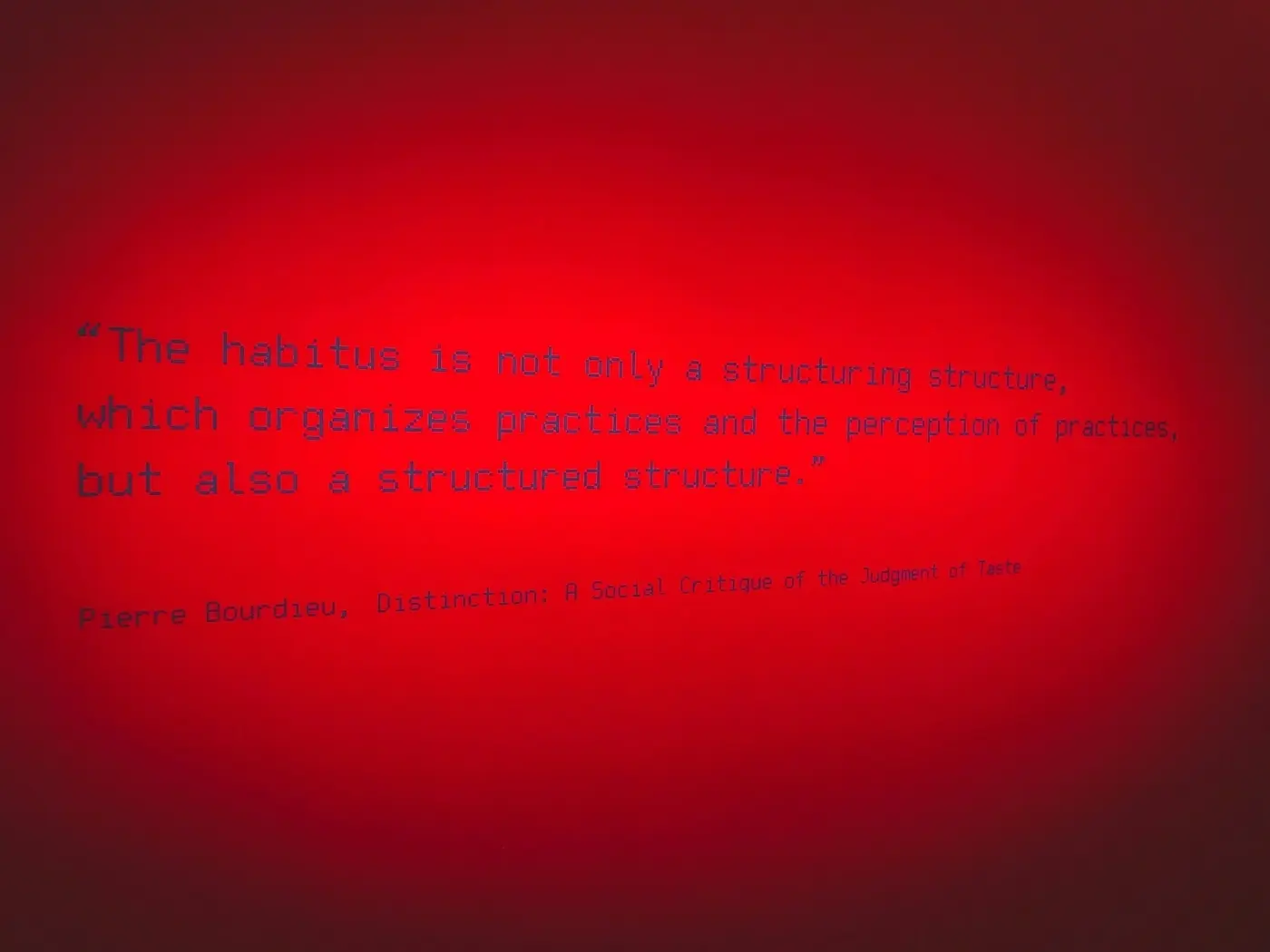 A red wall displays a quote by Pierre Bourdieu about habitus being both a structuring structure and a structured structure.