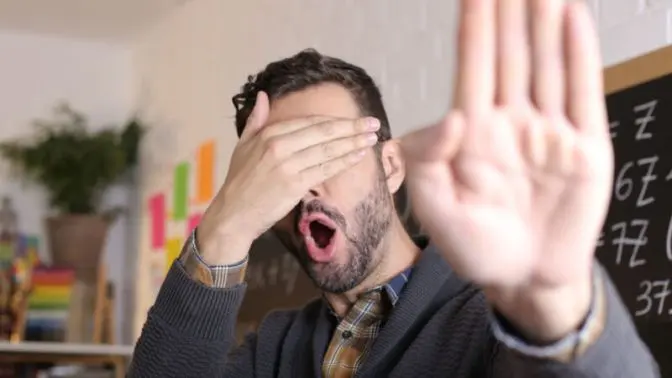 Person covering their eyes with one hand and making the 'stop' sign with the other.