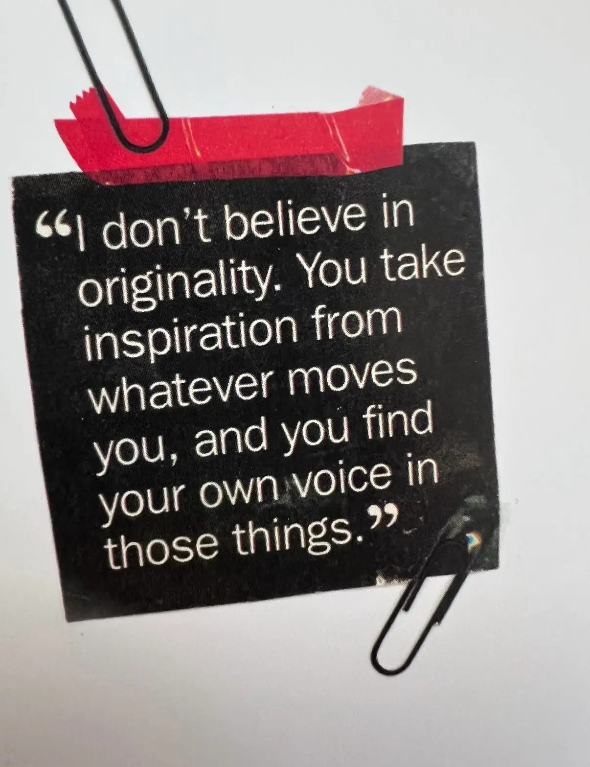 Auto-generated description: A quote about finding inspiration and individuality is attached to a surface using red tape and paperclips.
